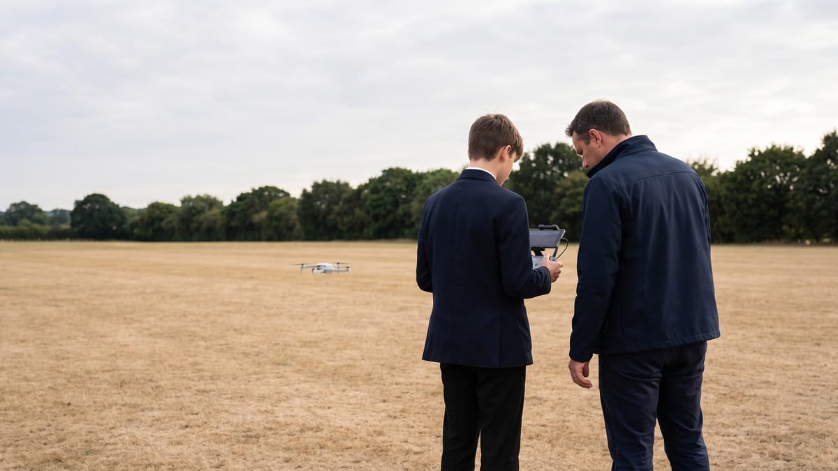 Un adulto e un ragazzo di spalle in un parco osservano un piccolo drone in volo
