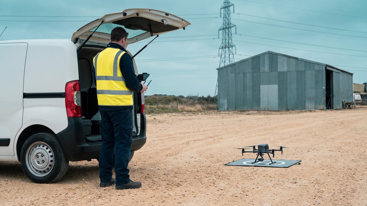 Operatore di spalle con gilet ad alta visibilità accanto a un drone professionale pronto al decollo